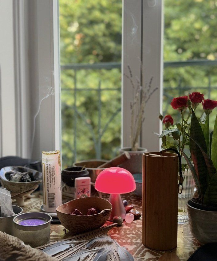 Altar montado junto à janela, com velas, flores e elementos naturais